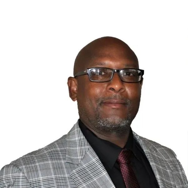 A man in a suit and tie standing up against a white wall.