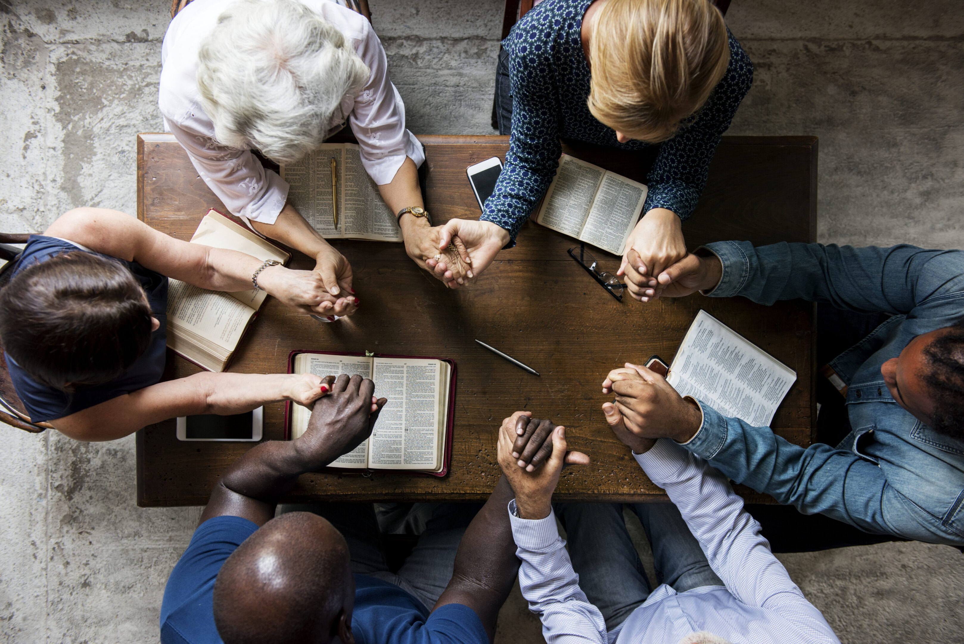 A group of people sitting around a table with hands folded in prayer.